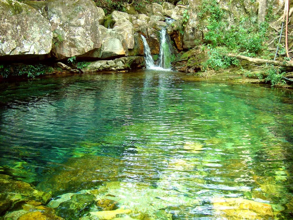 Poço de água transparente na Fazenda Loquinhas, com o leito de pedra visível no fundo e mata nas margens