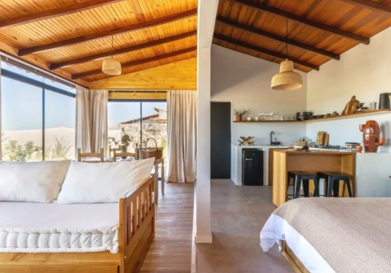 Ambiente integrado: sofá bicama, cozinha com banquetas e a cama, sob o teto de madeira