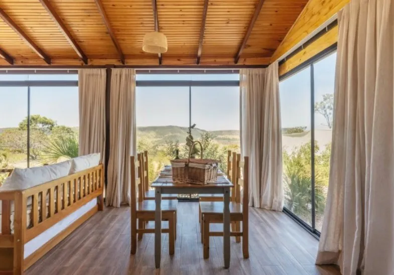 Mesa de jantar para quatro com cesta de piquenique, diante das janelas com vista das serras
