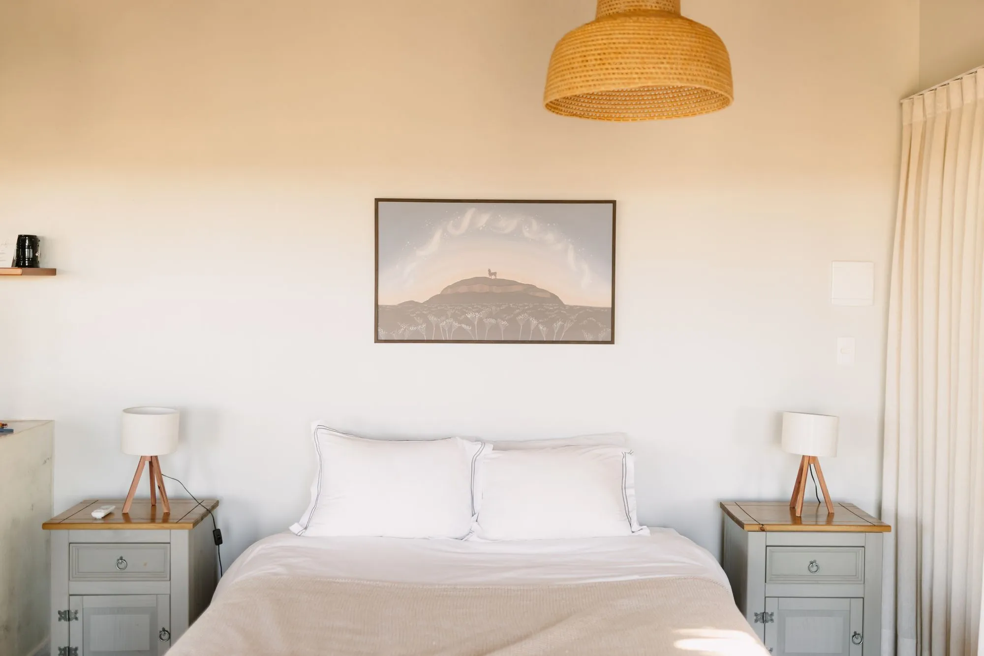 Cama queen entre dois criados-mudos com abajures e um quadro das montanhas na parede