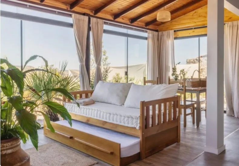 Sofá bicama de madeira com a segunda cama puxada, sob o teto de madeira aparente