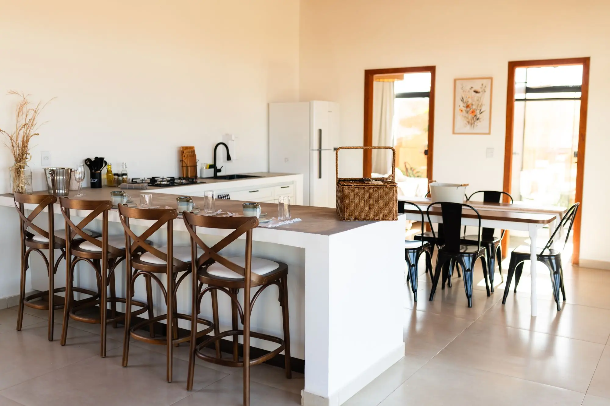 Cozinha com balcão, quatro banquetas, geladeira e mesa de jantar