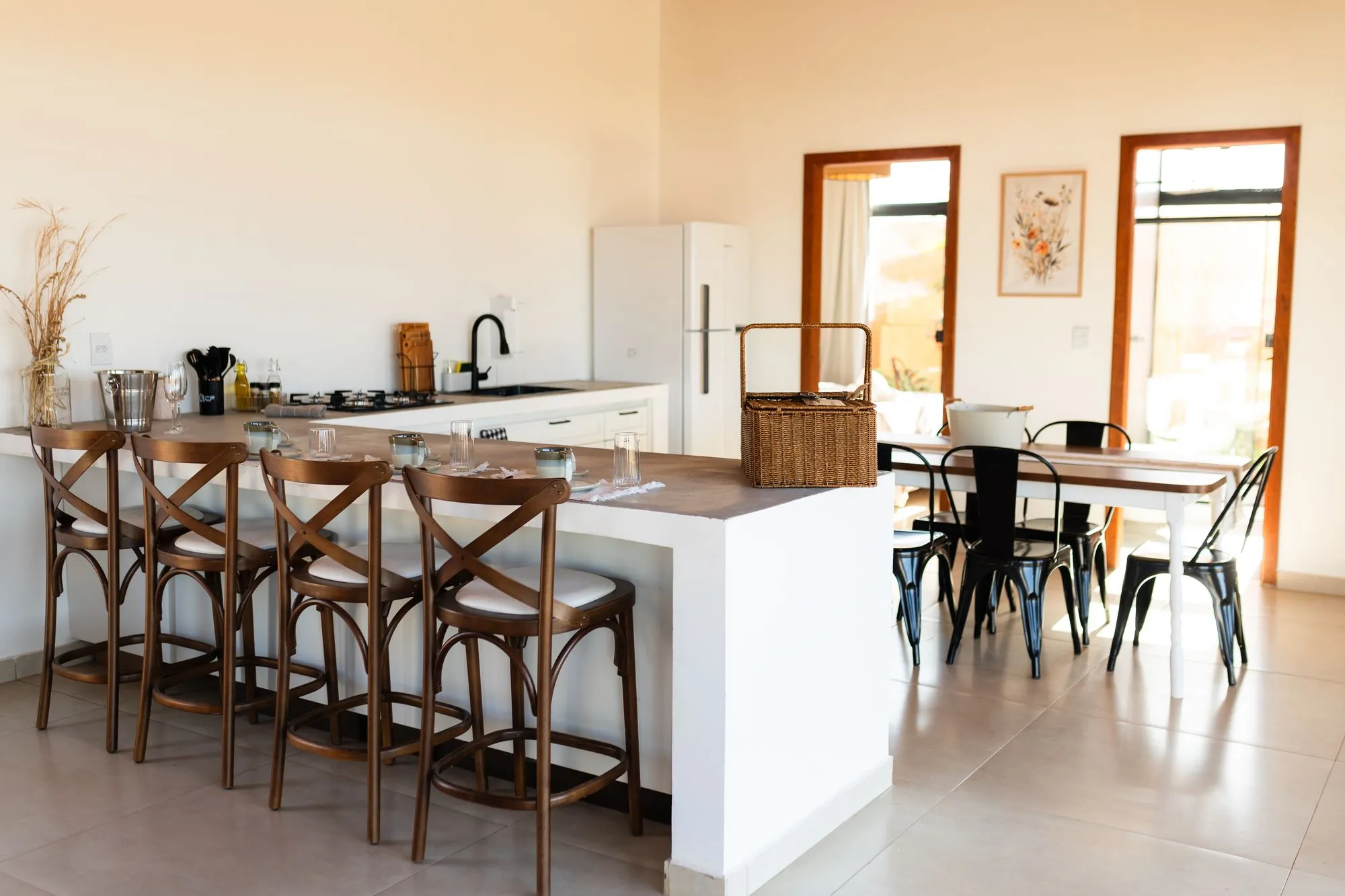 Cozinha com balcão, quatro banquetas, geladeira e mesa de jantar