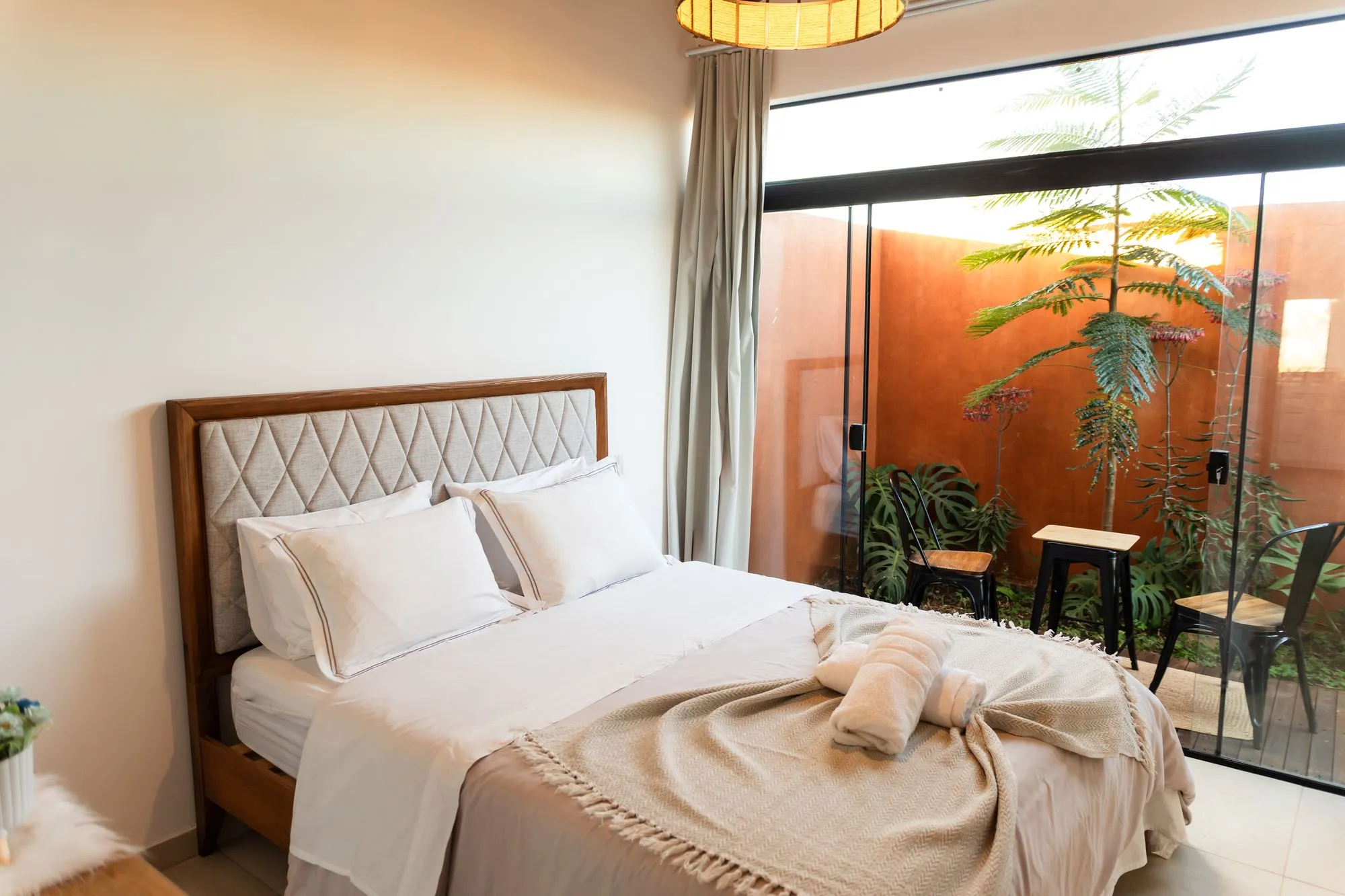 Primeiro quarto: cama queen com cabeceira estofada e parede de vidro para um pátio com plantas