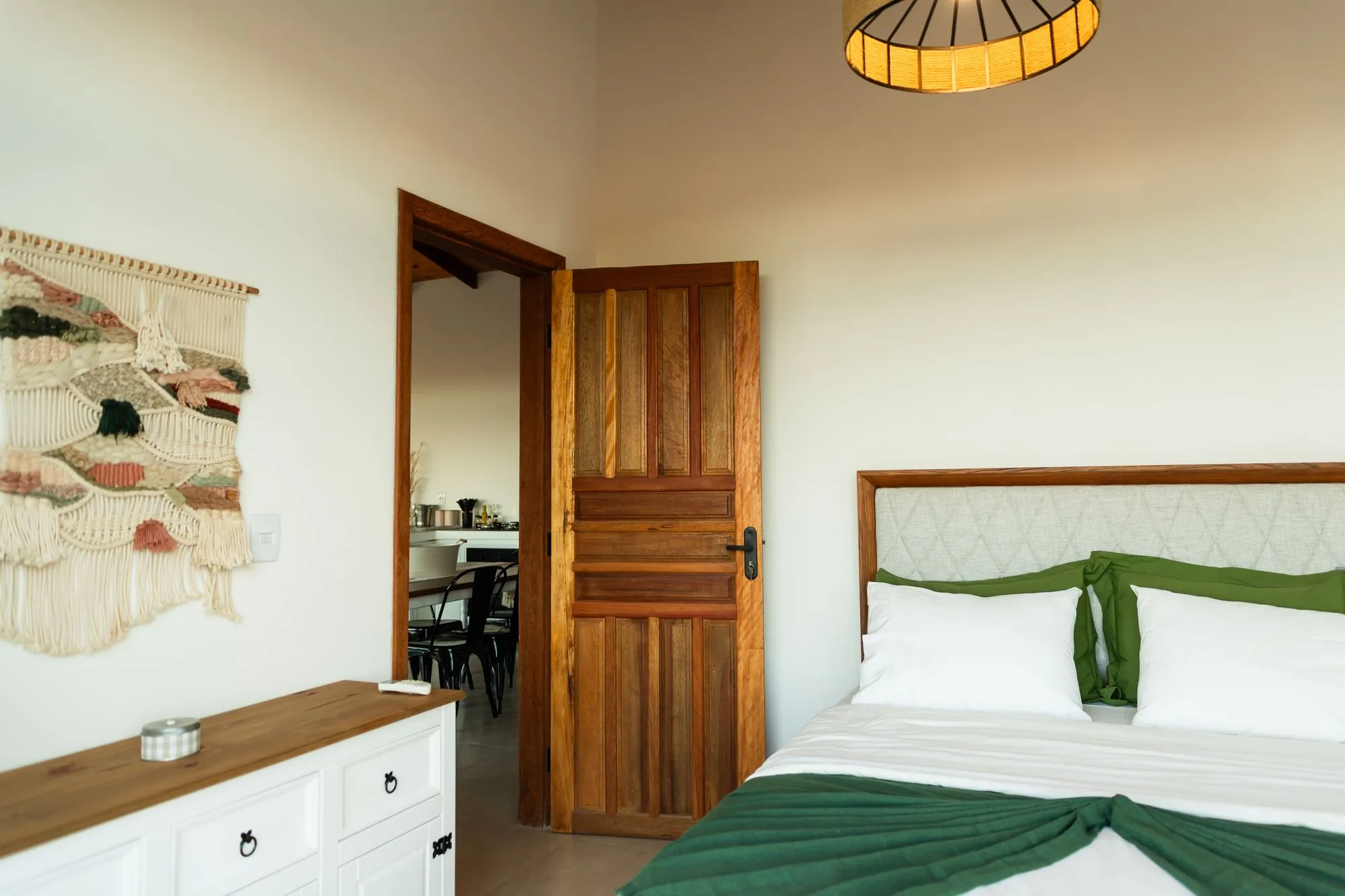Segundo quarto: cama queen com manta verde, macramê na parede e porta de madeira
