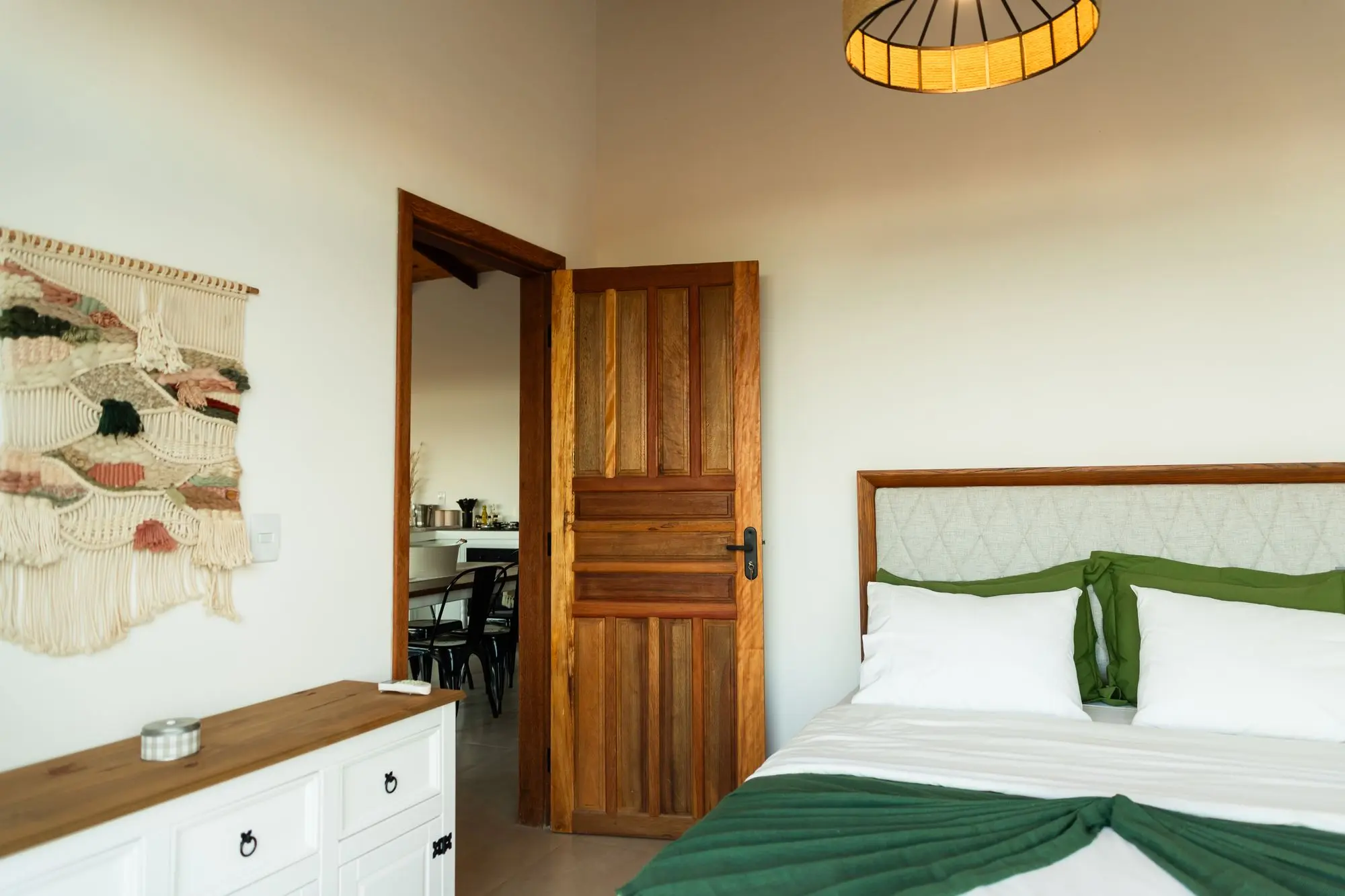 Segundo quarto: cama queen com manta verde, macramê na parede e porta de madeira