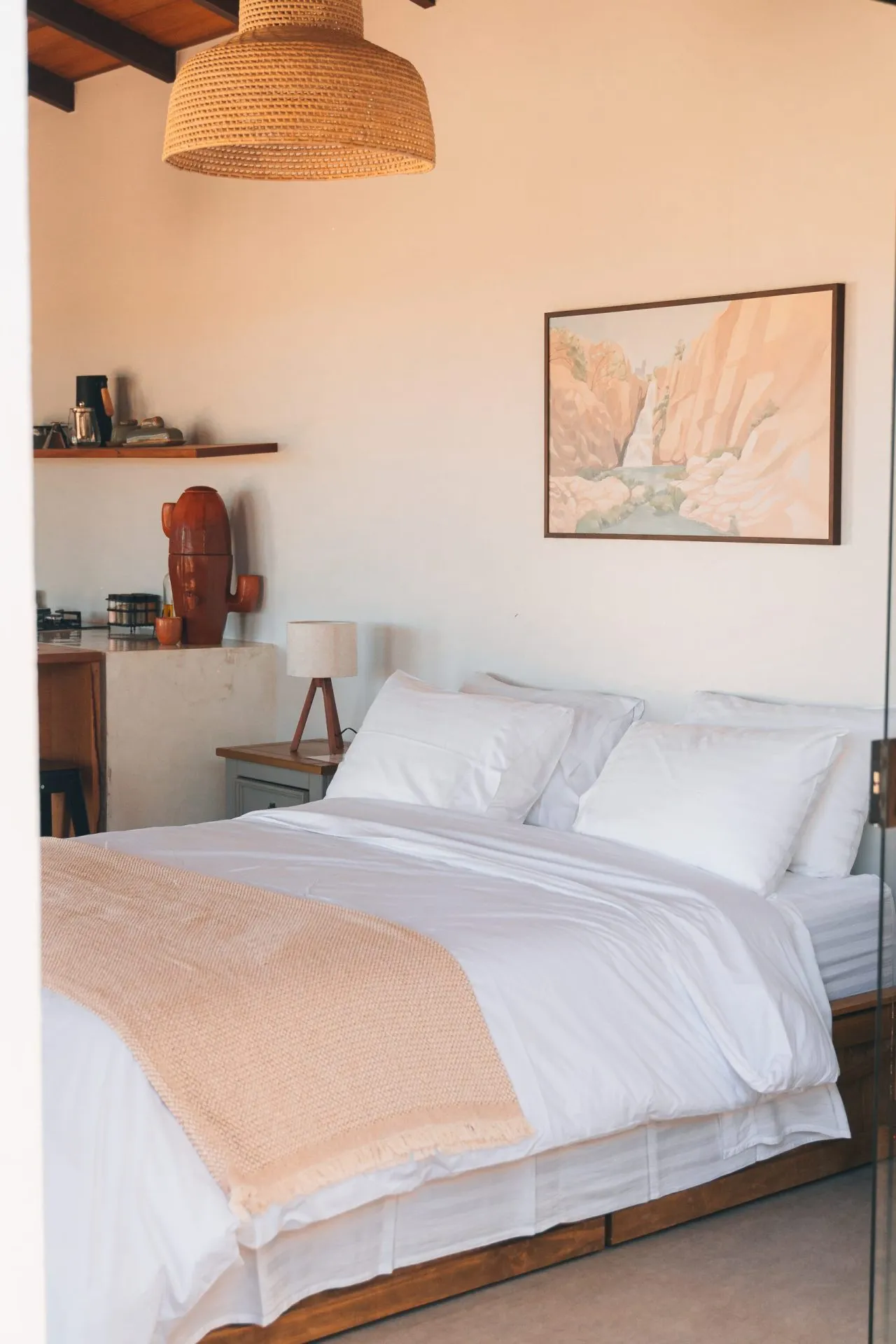 Chalet bedroom with a king bed in white linens, a rattan pendant light, a landscape print and a wooden headboard