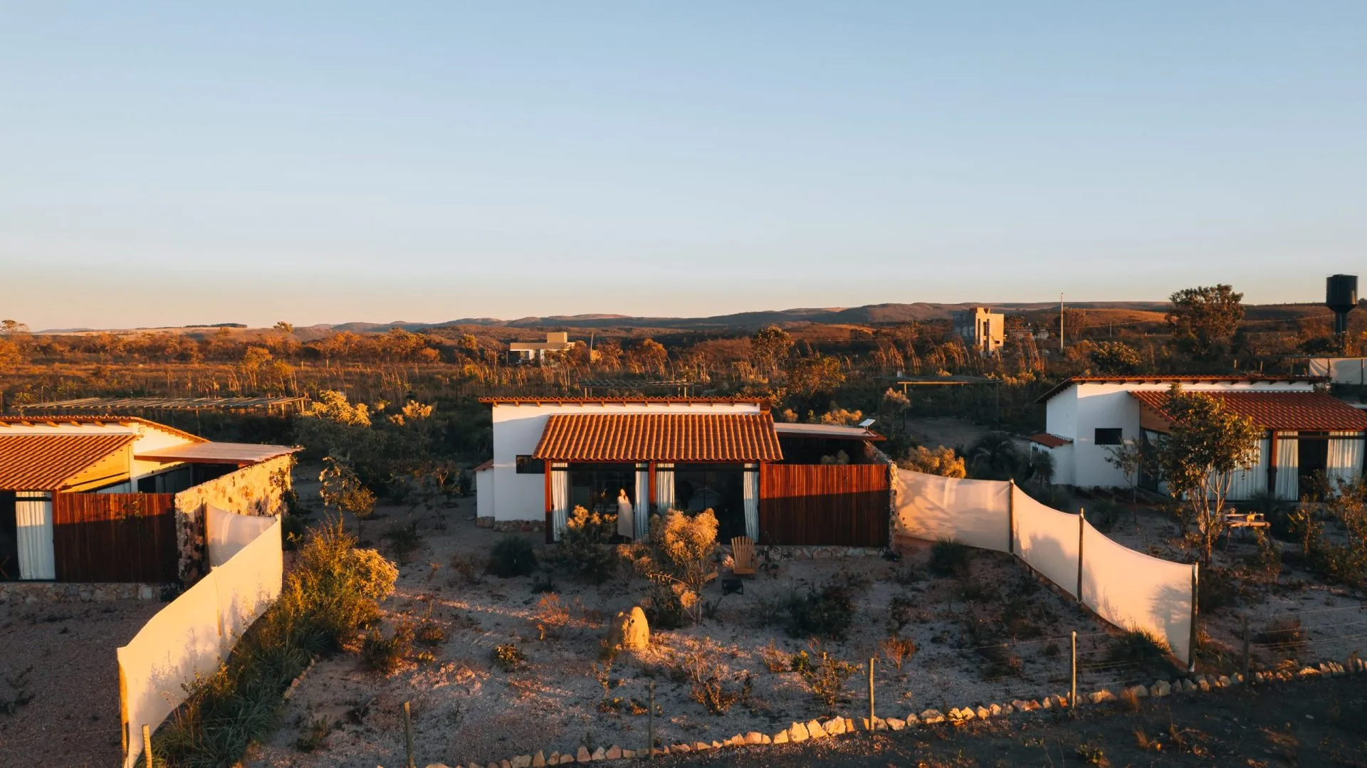 Aerial view of the Paradise Ranch chalets bathed in golden sunset light, with Cerrado vegetation beyond