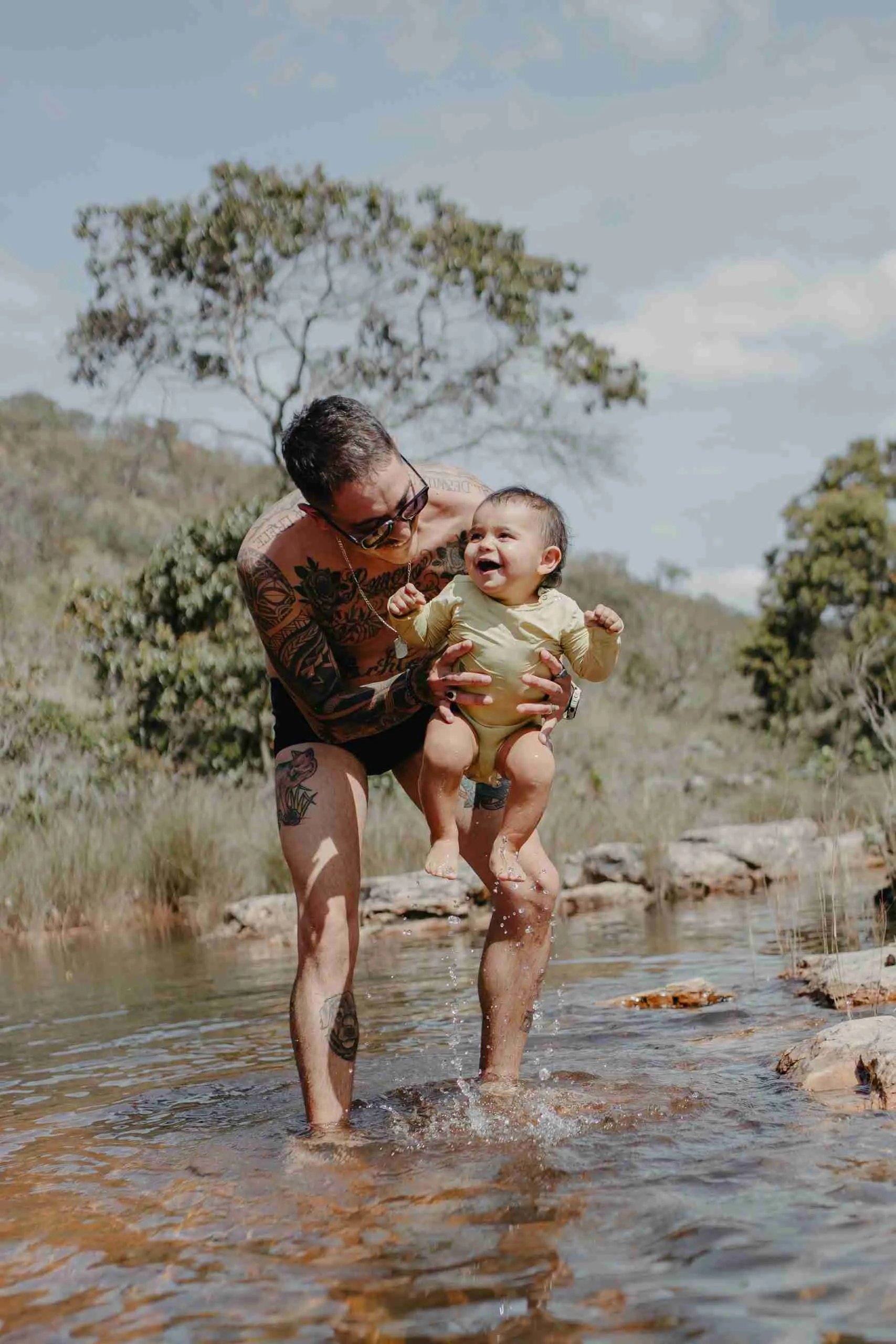 Pai erguendo bebê sorridente sobre as águas cristalinas de rio no Cerrado